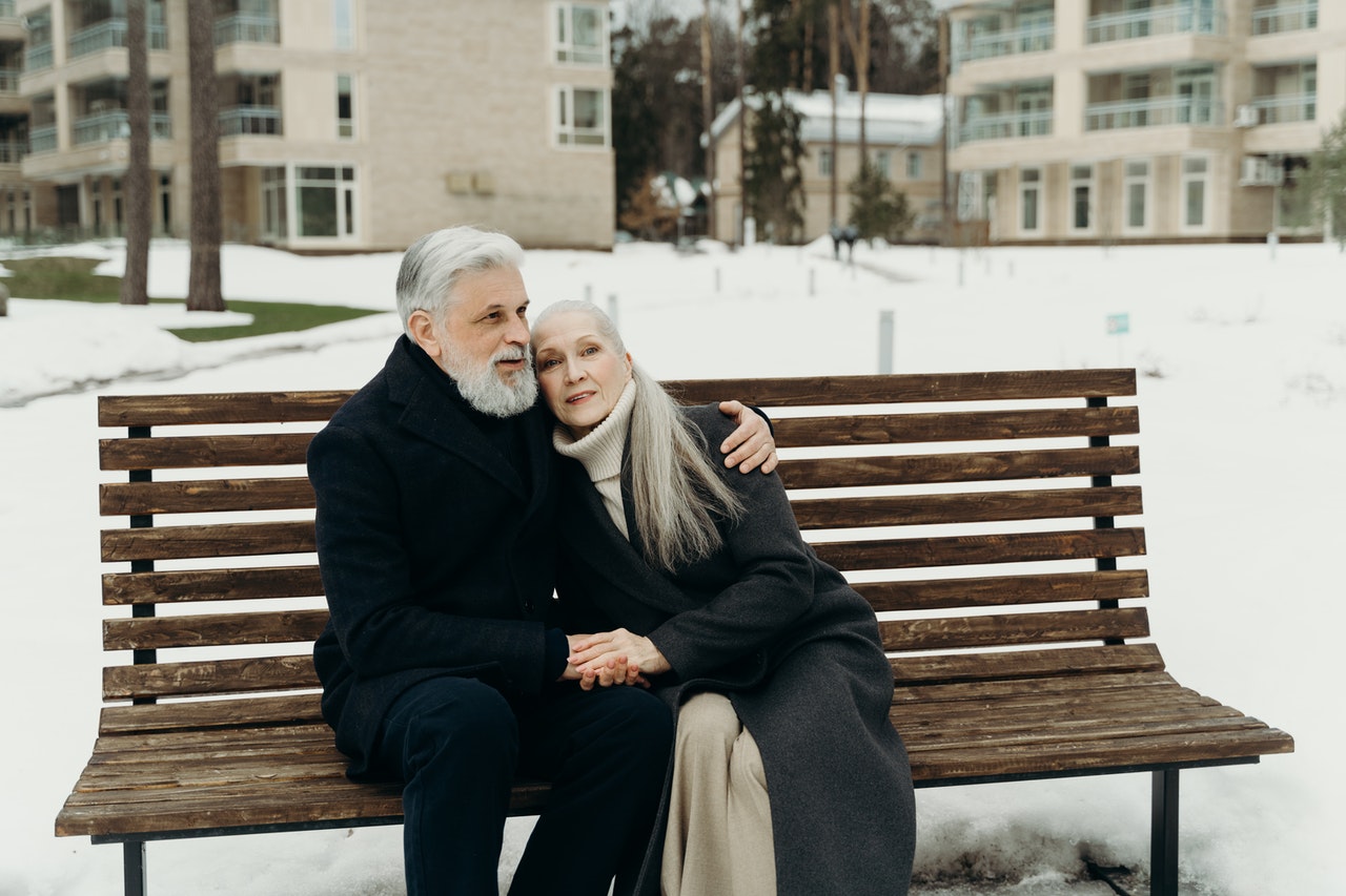 An old couple wearing dark-colored coats while sitting on the bench