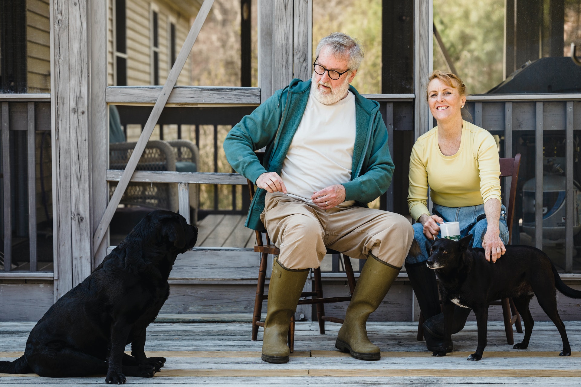 A couple wearing rubber boots while petting their two black dogs