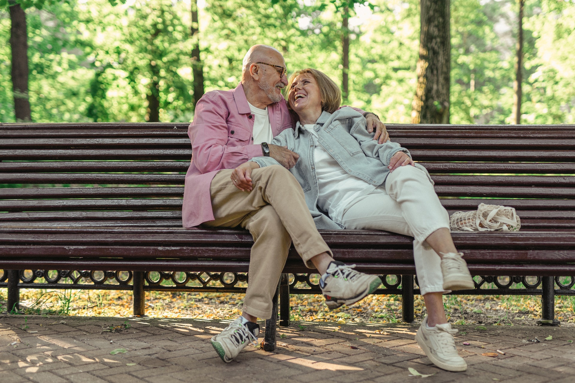 A couple wearing light-colored denim jackets and jeans while sitting on a bench